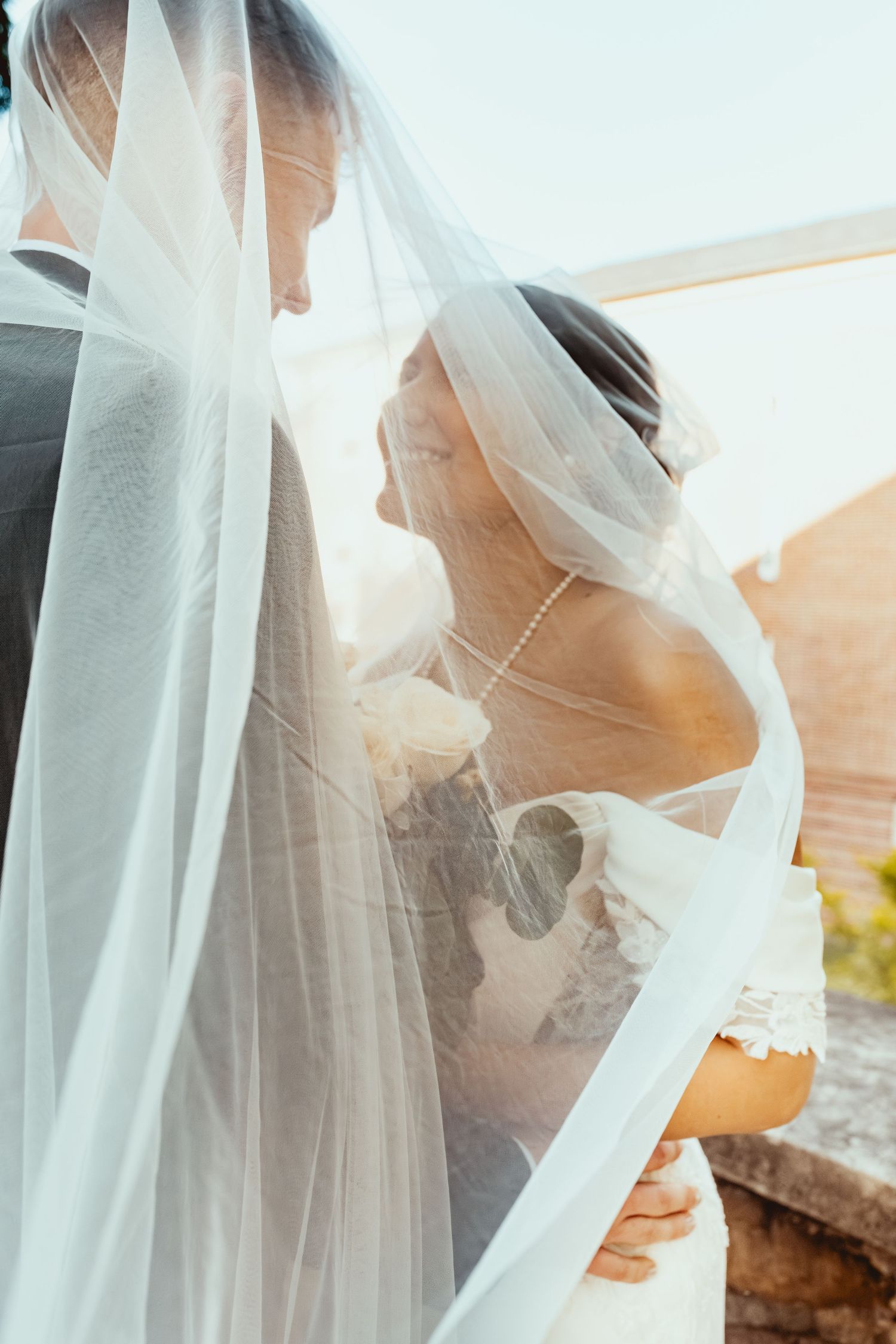 A romantic wedding scene with flowing white veil catching sunlight during an intimate outdoor moment.