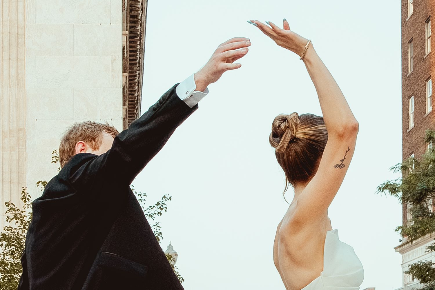 Two dancers in black and white outfits reaching upward with graceful arm movements against an urban backdrop.
