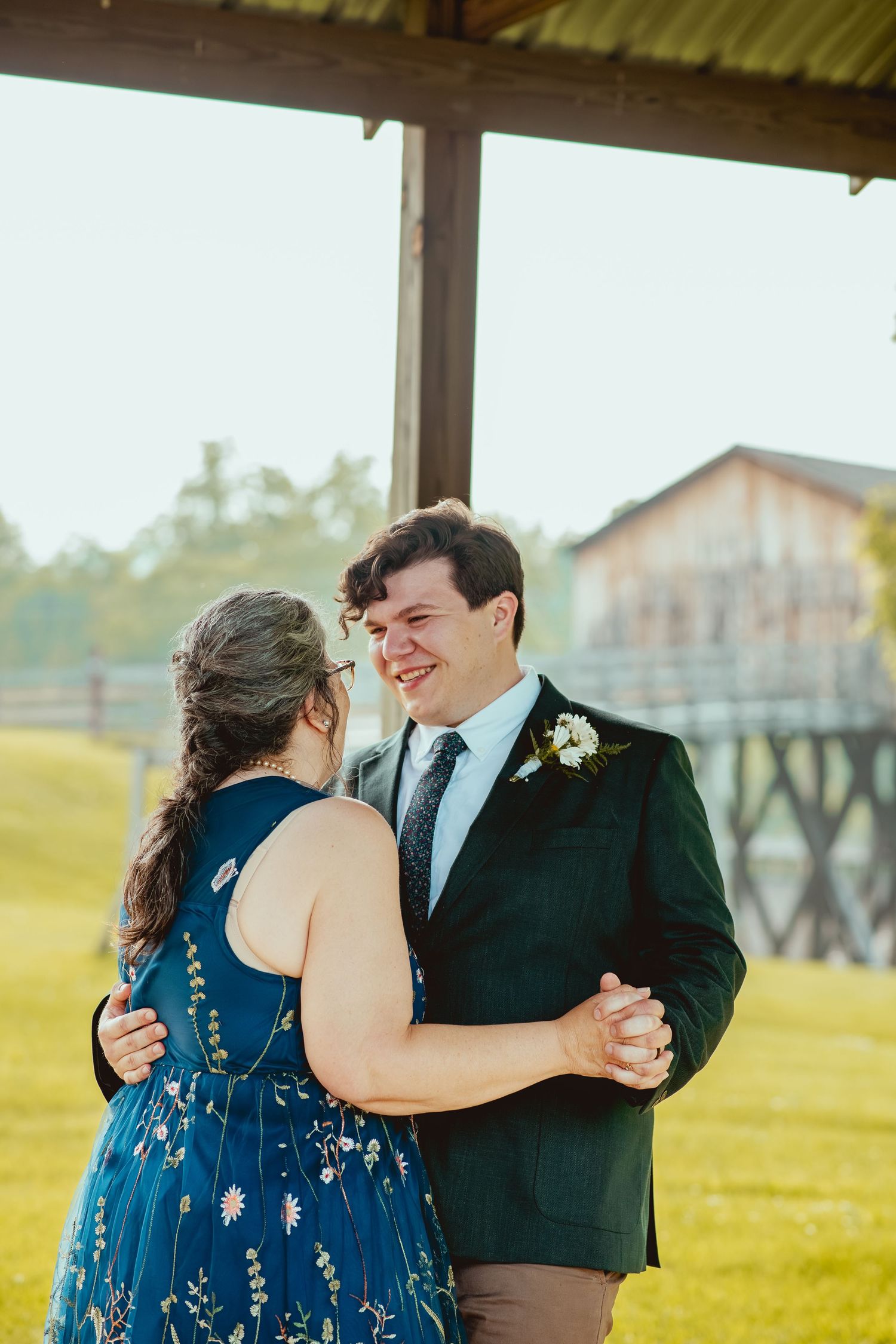 Couple dancing together in formal attire with navy blue dress against green outdoor backdrop.