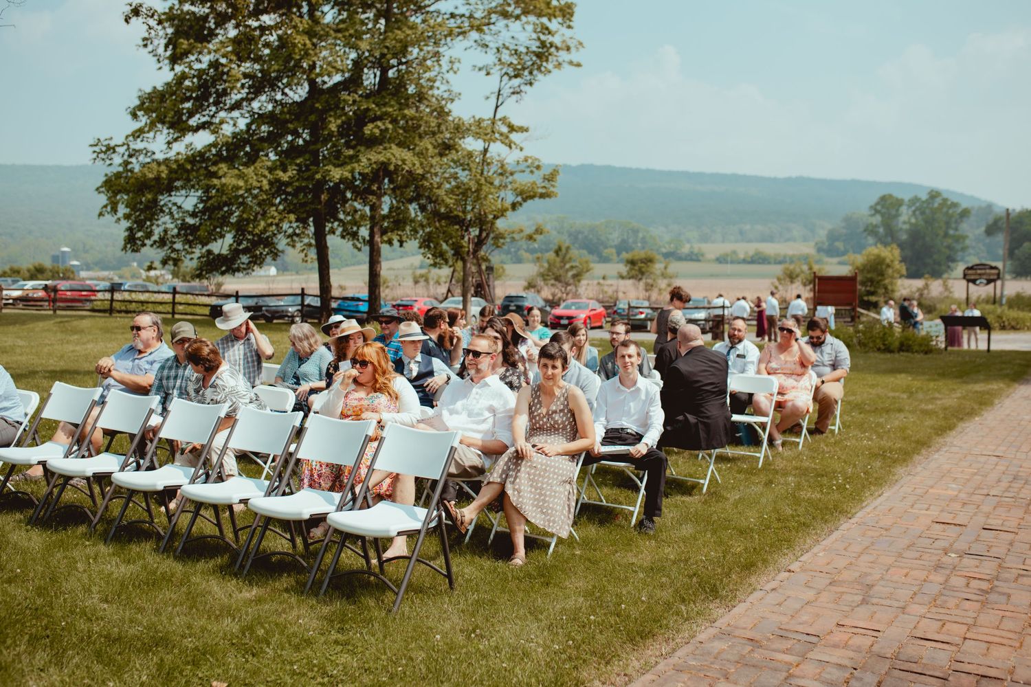 Guests seated in white chairs on a grassy hillside for an outdoor wedding ceremony with mountain views in the distance.
