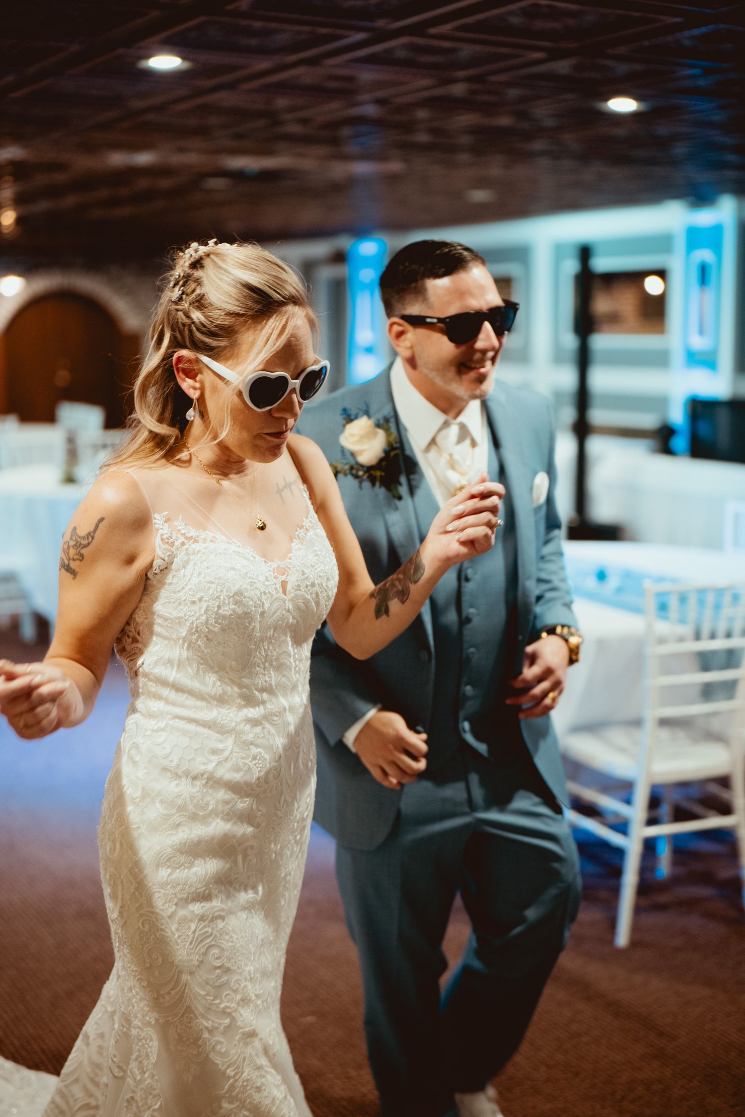 Wedding couple dancing in a reception hall wearing sunglasses and formal attire.