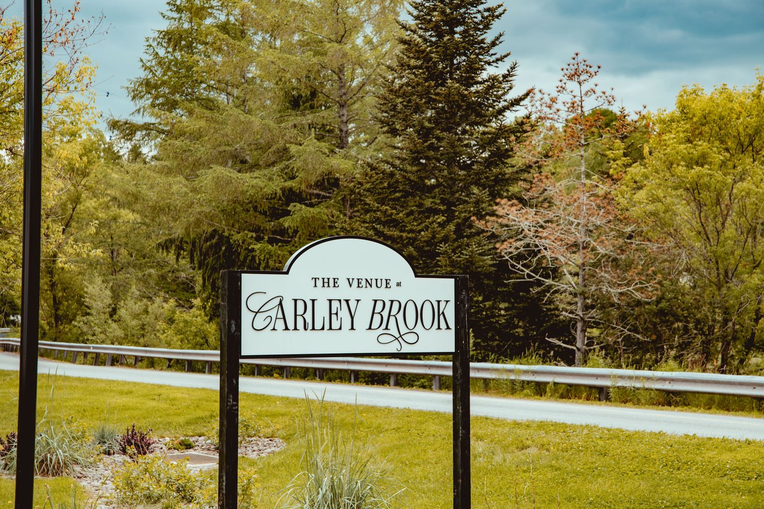 Carved wooden welcome sign for Carley Brook venue with evergreen trees in background.
