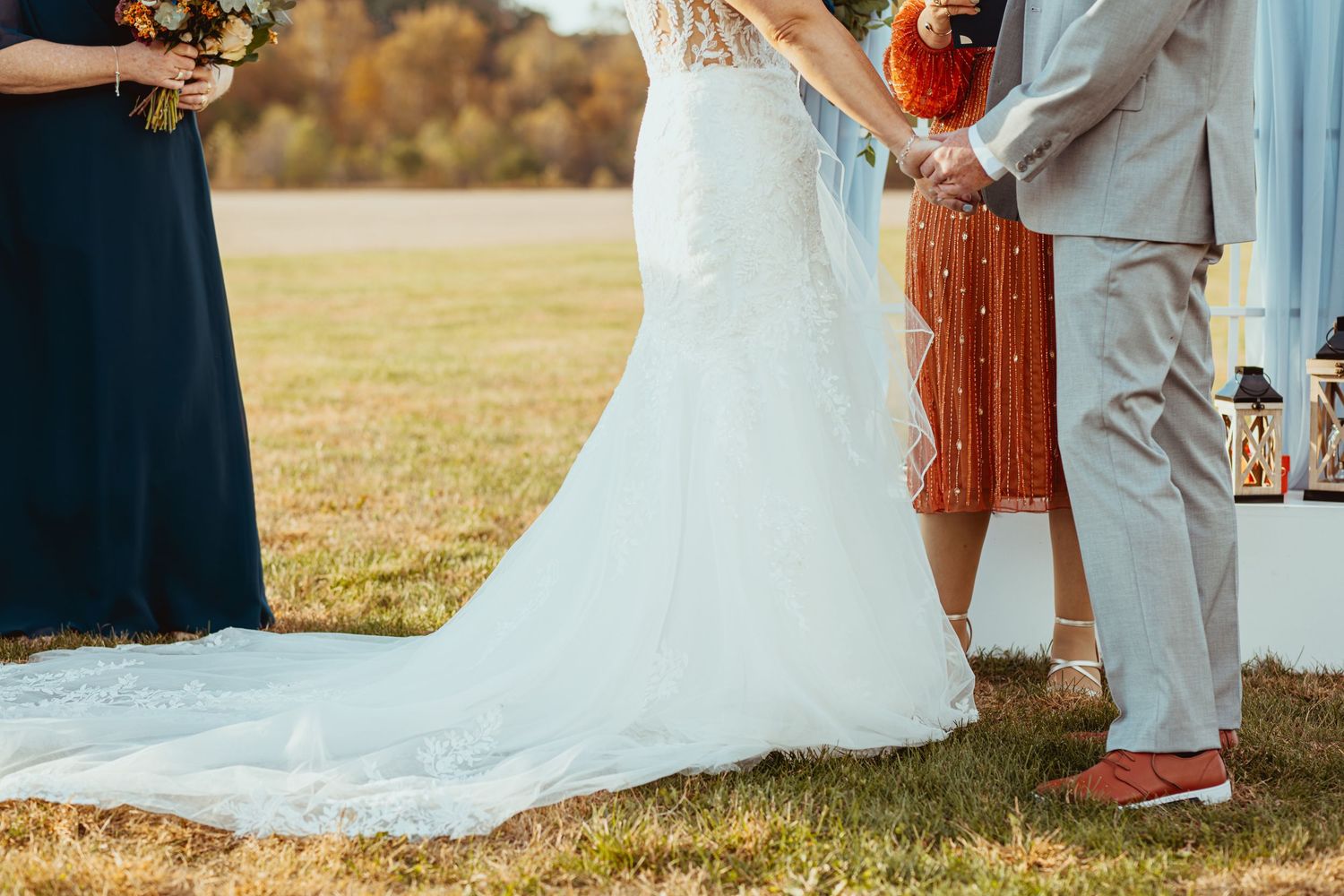 Outdoor wedding scene with white dress and light colored suits against a natural landscape background.