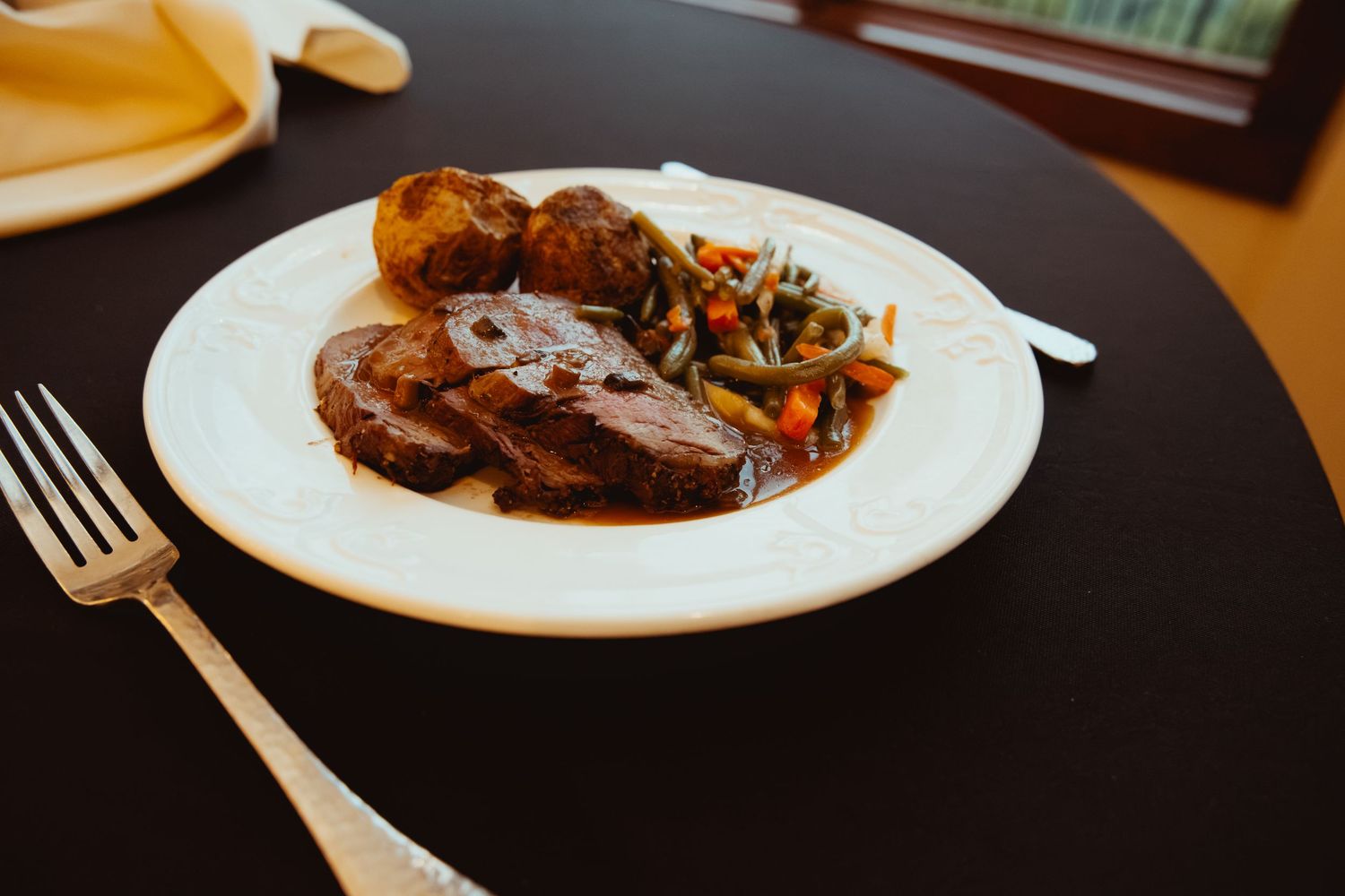 Elegant wedding reception dinner plate with braised meat, roasted vegetables, and potato on white china.