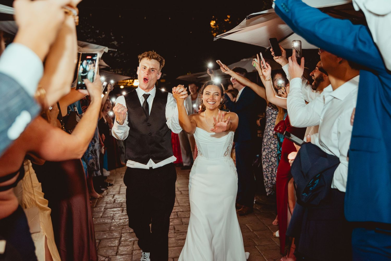 Wedding celebration on dance floor with guests in formal attire dancing under evening lights.