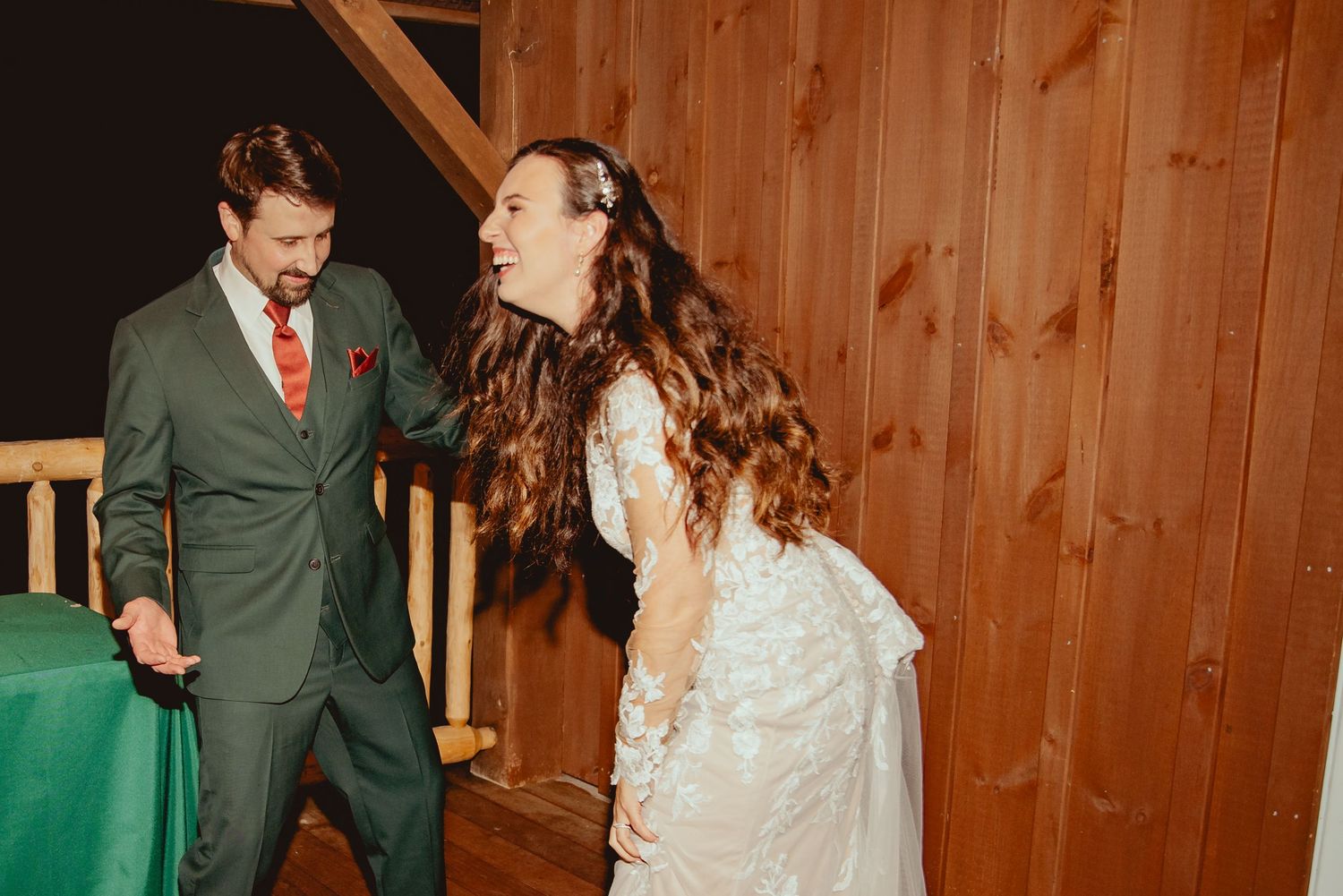 Couple shares joyful laughter during their wedding celebration in a rustic wooden venue.