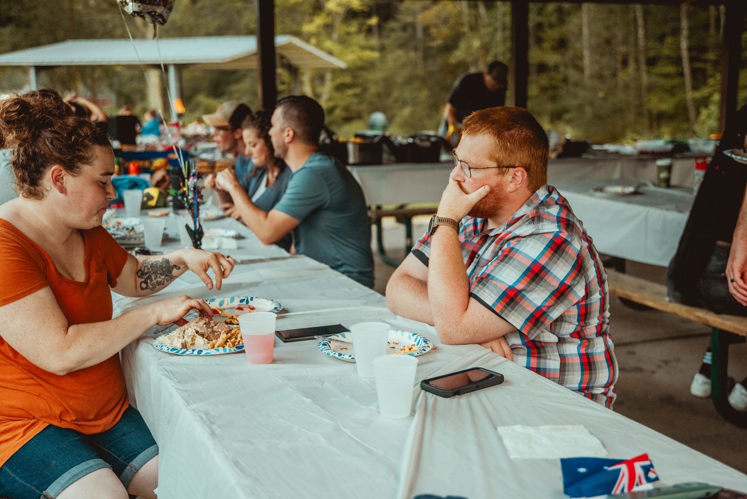 Group of people sitting at outdoor tables participating in a crafting or art activity together.