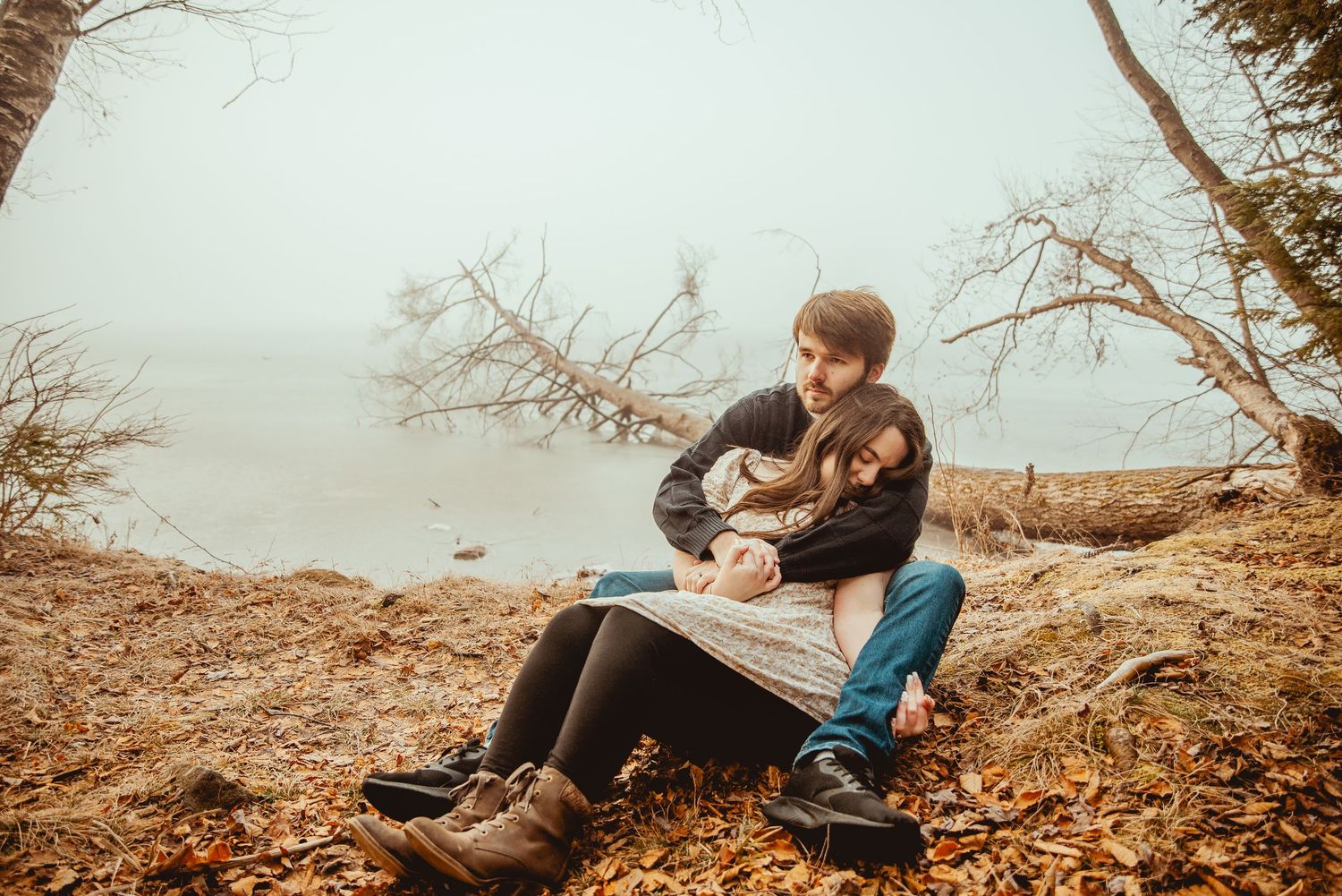 Romantic couple embraces while sitting on fallen autumn leaves in a park during golden hour.