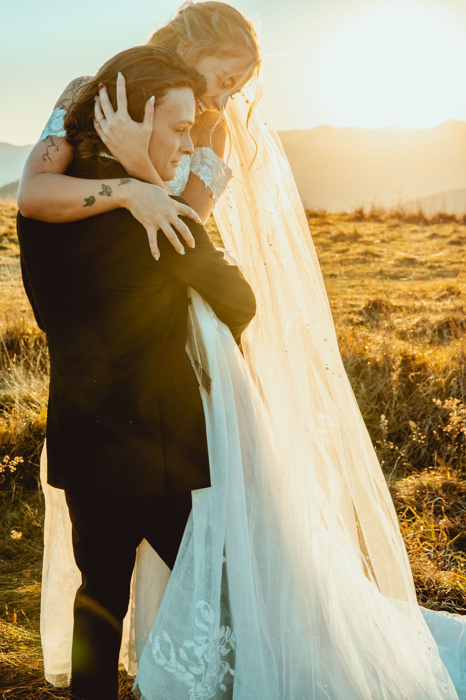 Romantic sunset wedding moment with flowing white dress against mountain backdrop.