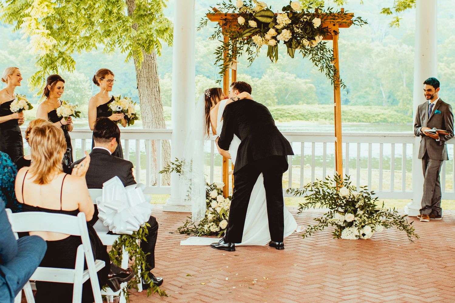 Outdoor wedding ceremony setup with floral arch and white chairs on a sunny patio.