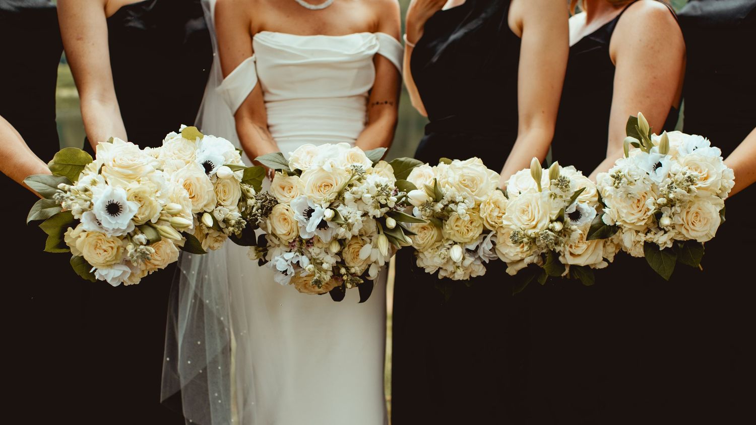White floral bouquets held against black dresses in a wedding party lineup.