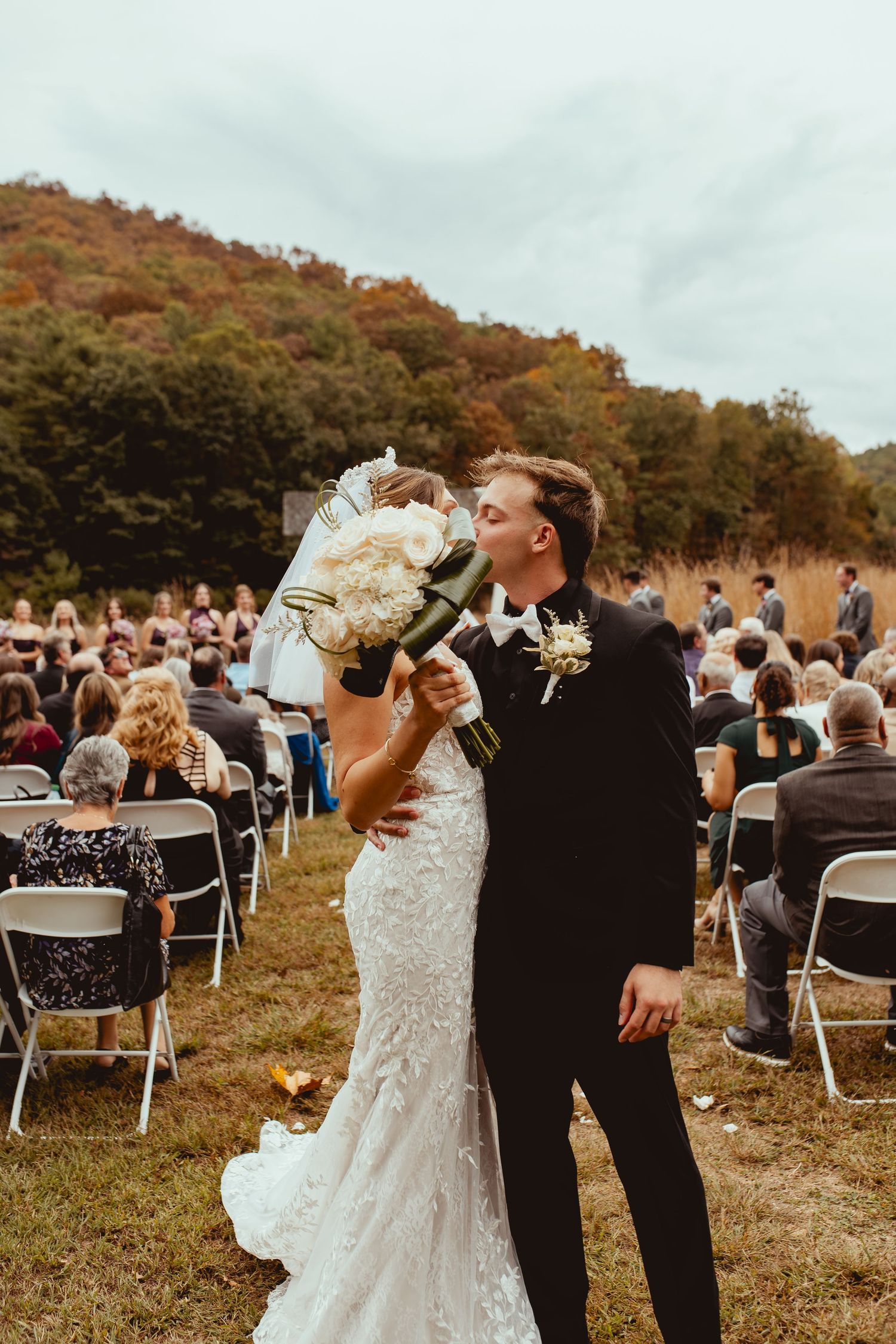 An outdoor wedding ceremony with white chairs set up on a hillside during autumn.
