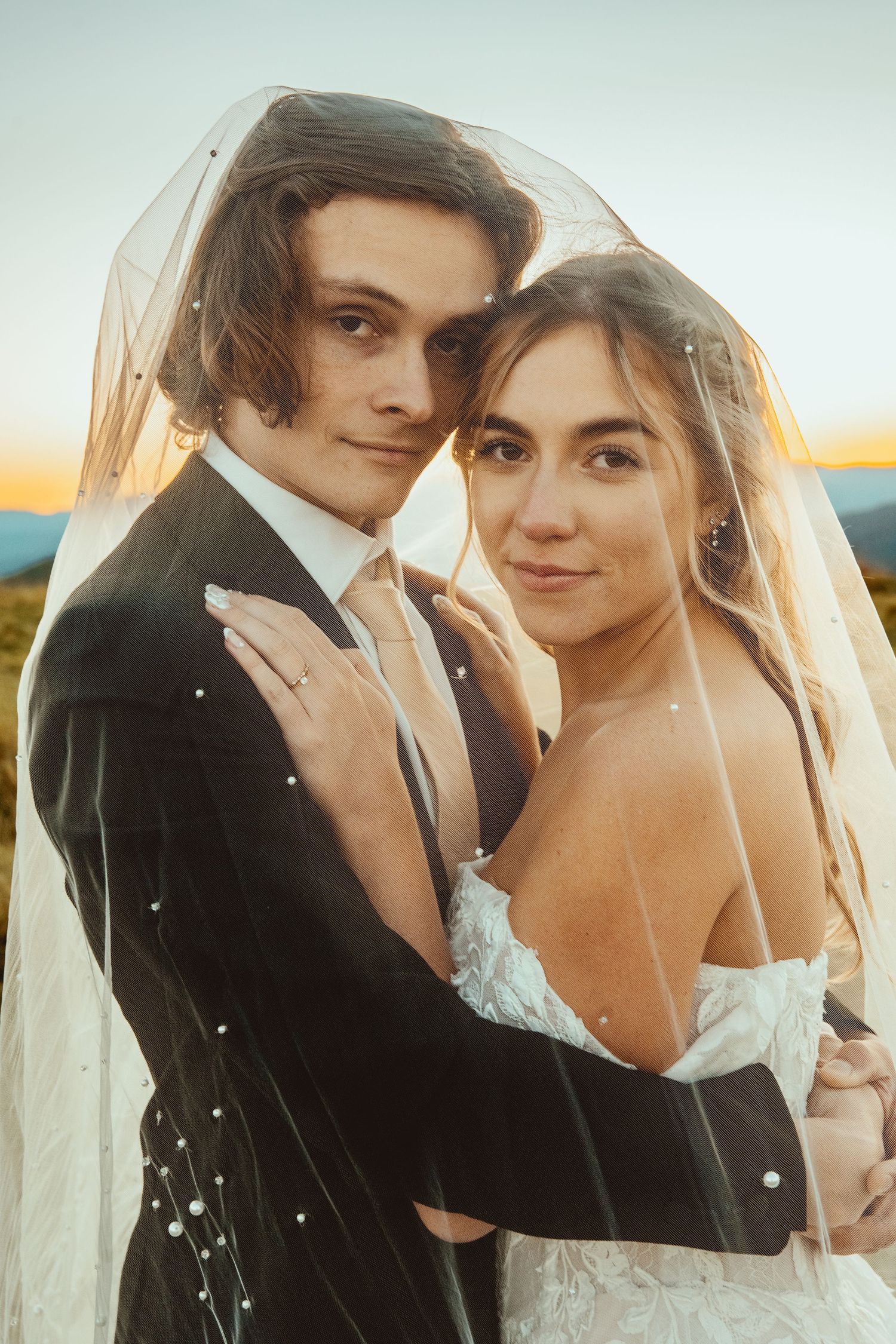 Intimate portrait of newlyweds under bridal veil during golden hour.