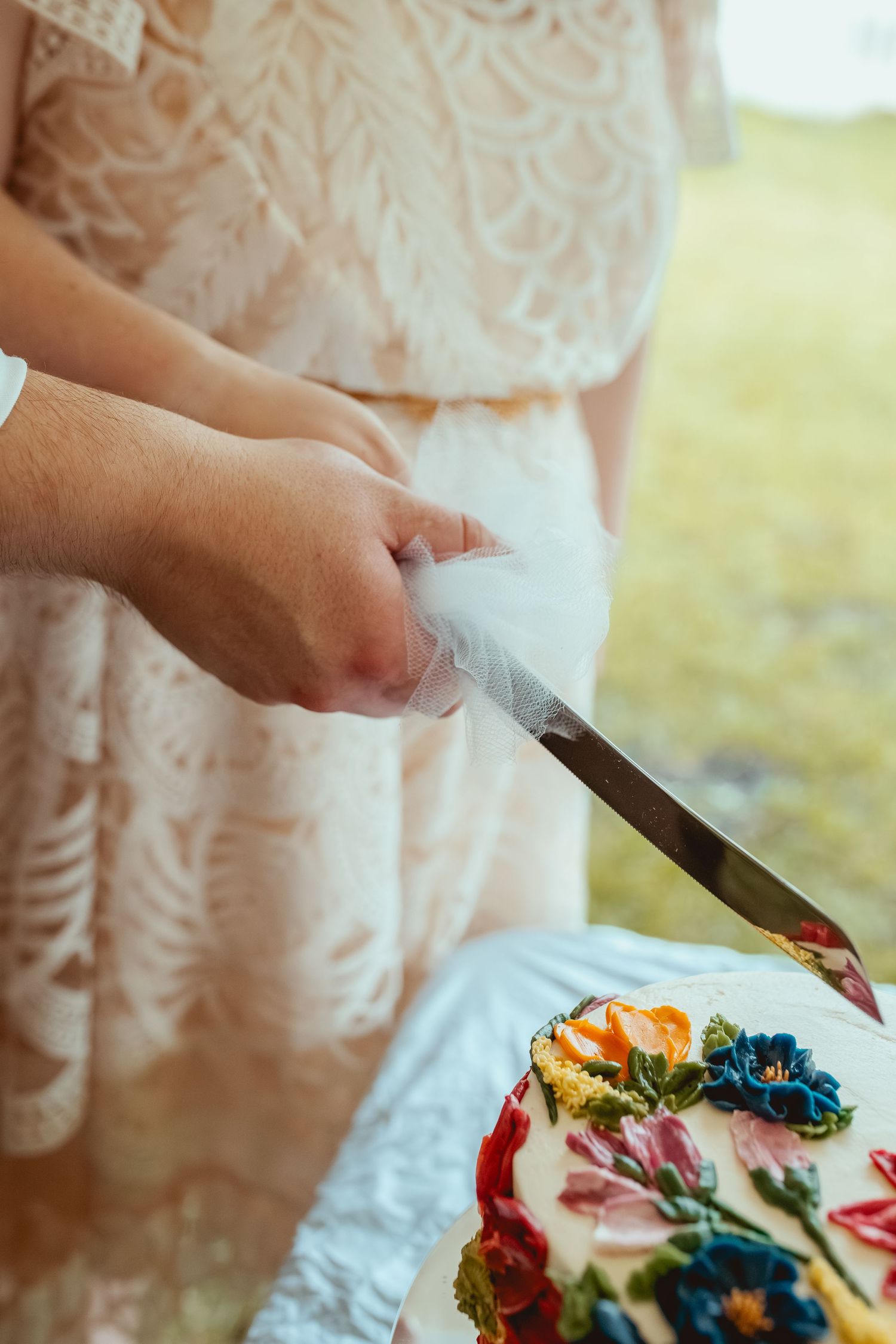 A couple shares a slice of colorful wedding cake decorated with bright flowers at their reception.