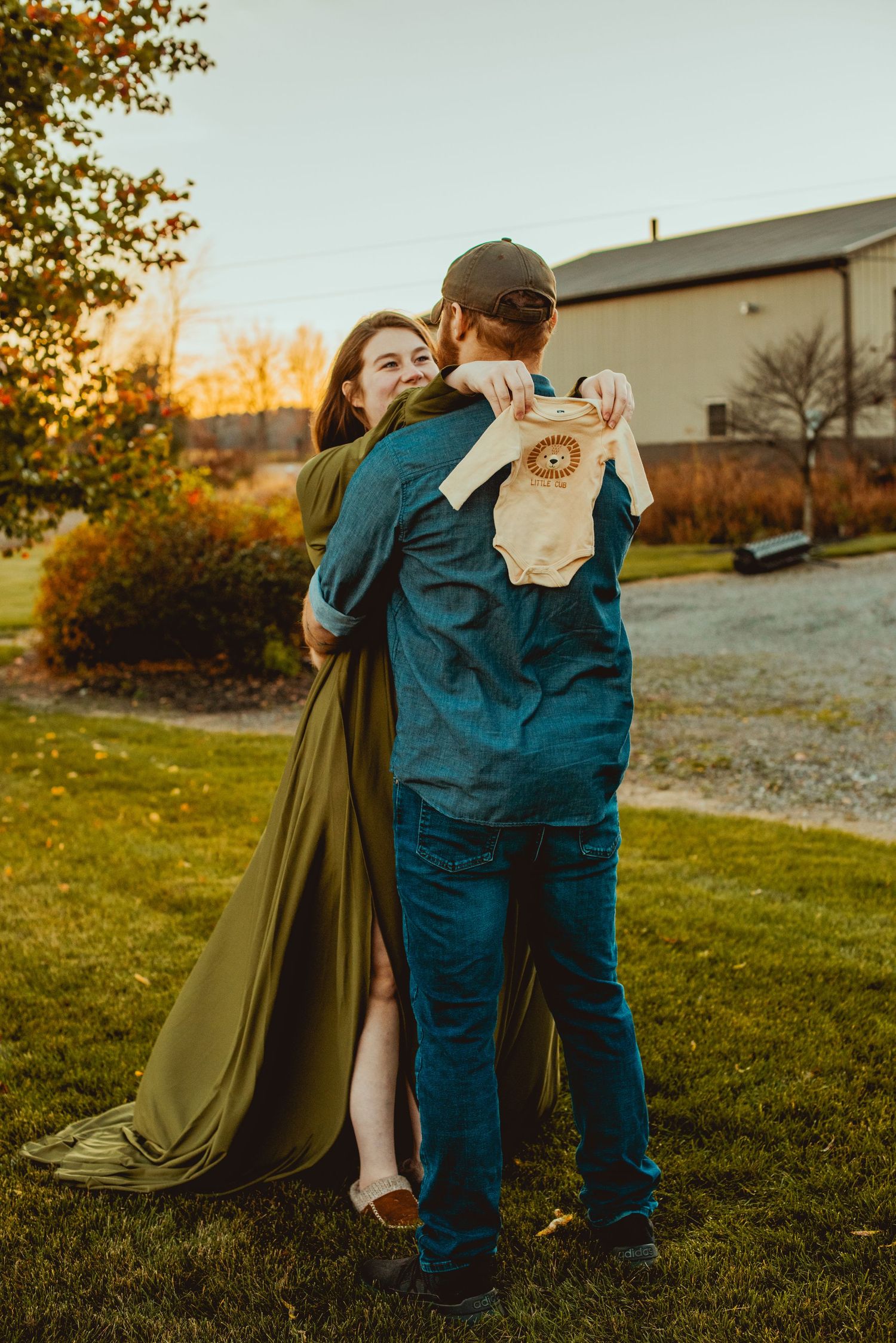 Two people share a tender embrace in matching teal outfits on a grassy field at golden hour.