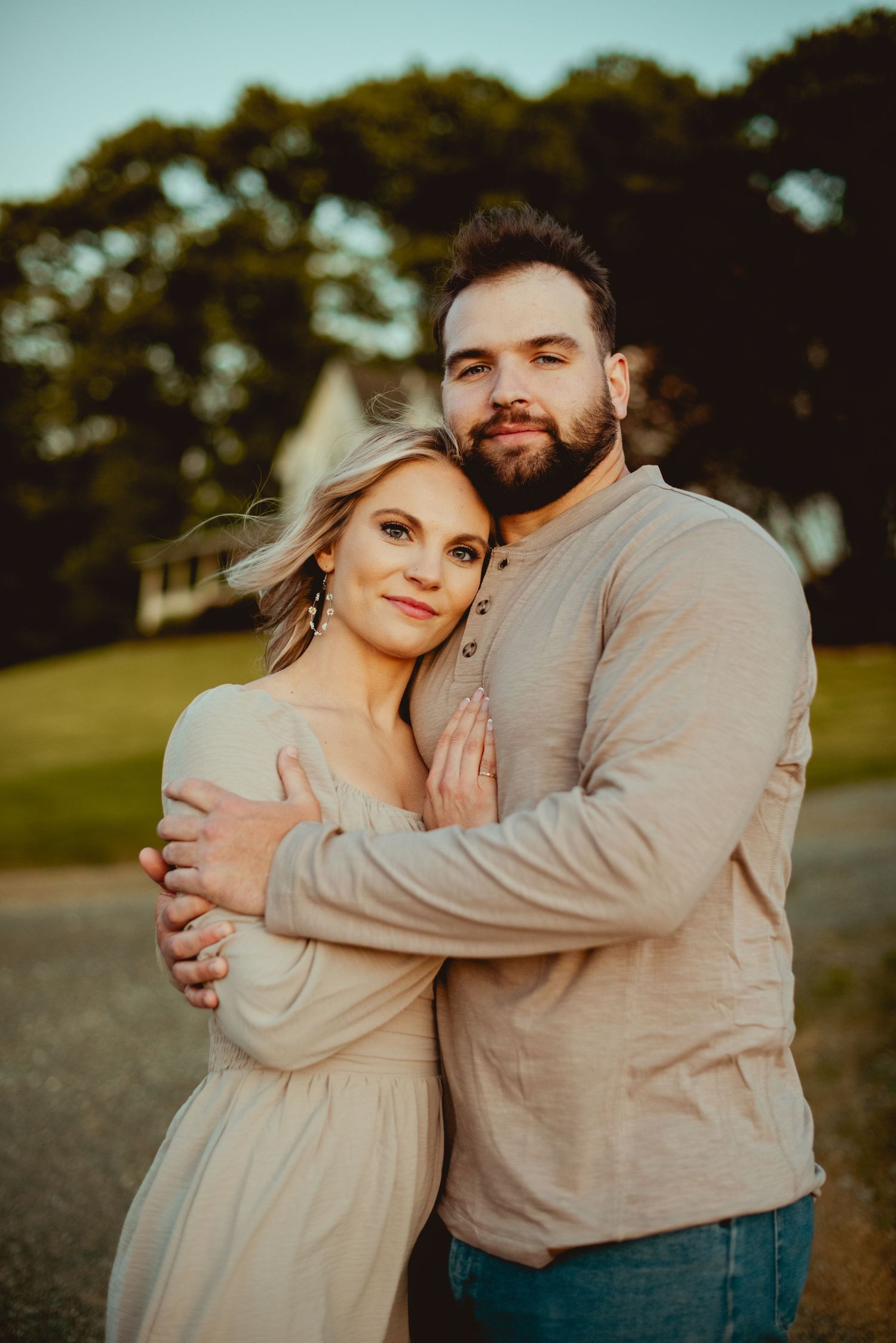 Couple in neutral tones embrace while sharing an intimate moment outdoors at sunset.