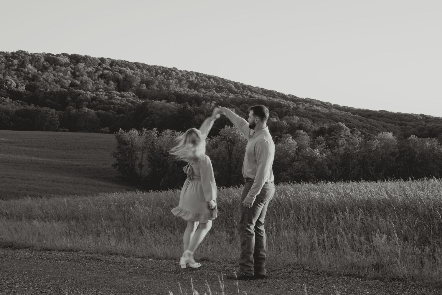 Black and white photo of two people walking through a scenic meadow landscape.