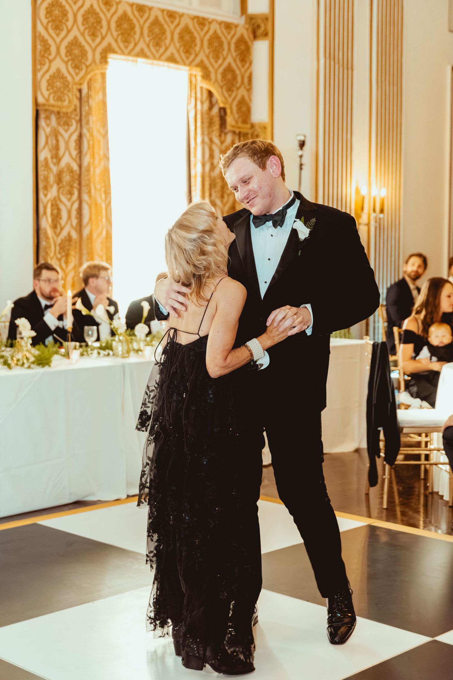 Elegant ballroom reception with ornate gold wallpaper and romantic lighting during a formal dance.
