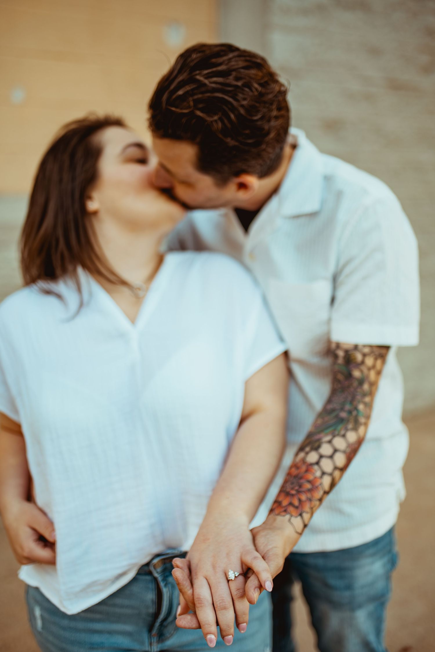 Couple kissing while holding hands, man with tattoo sleeve wearing white shirt.