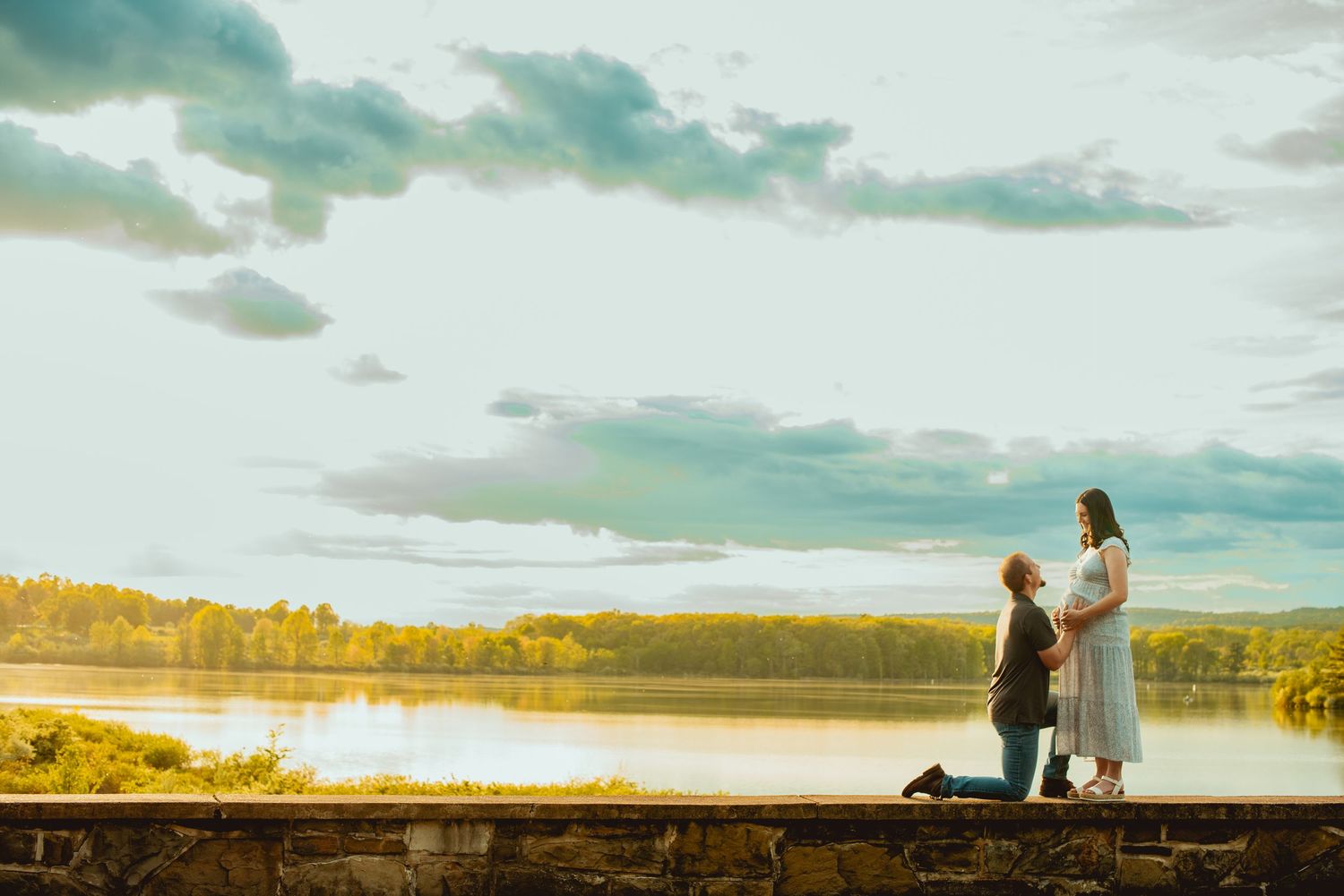 A couple stands silhouetted against a scenic autumn lake with dramatic cloudy sky at sunset.