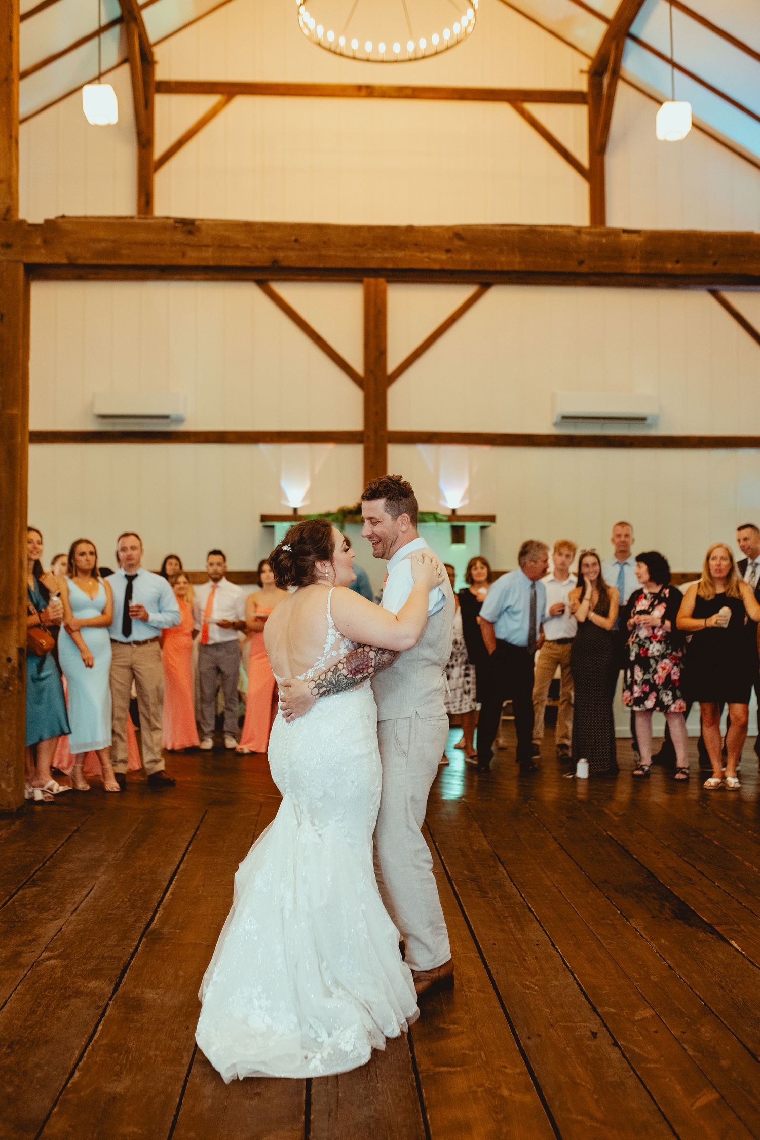 Bride and groom share first dance in rustic barn wedding venue surrounded by guests.
