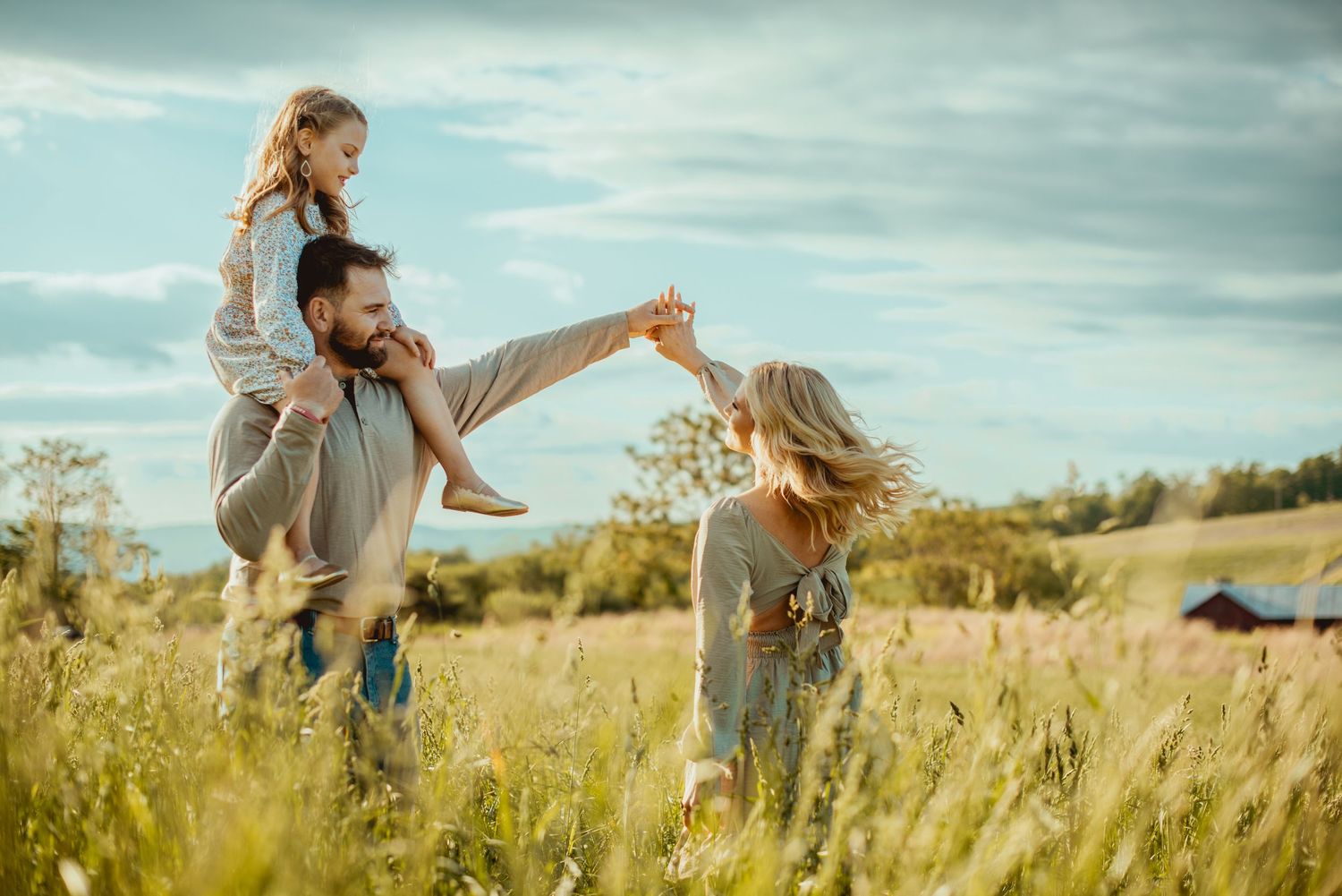 Family enjoying a playful moment while walking through a sunlit meadow on a cloudy day.