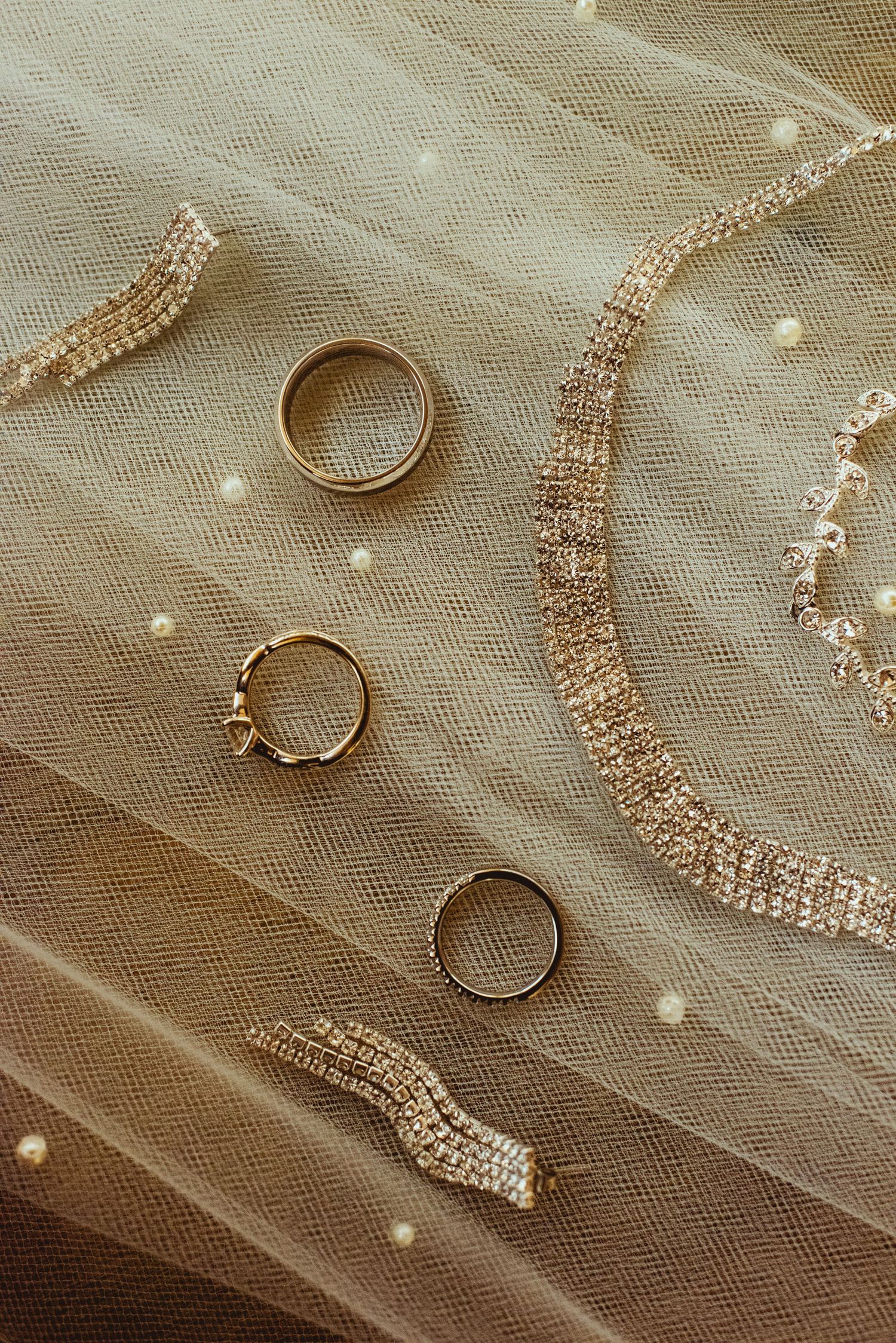Gold wedding rings and jewelry displayed on delicate white tulle fabric with sparkly details.