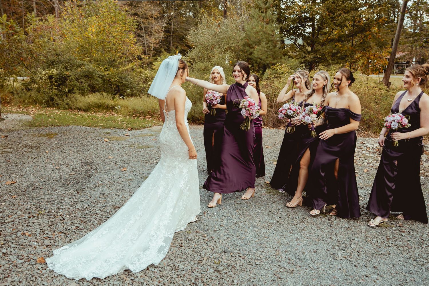Wedding party seated outdoors in purple dresses watching celebration on autumn day.