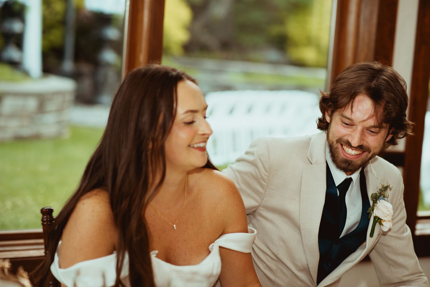 Bride and groom share a joyful laugh together while seated at their wedding reception table.