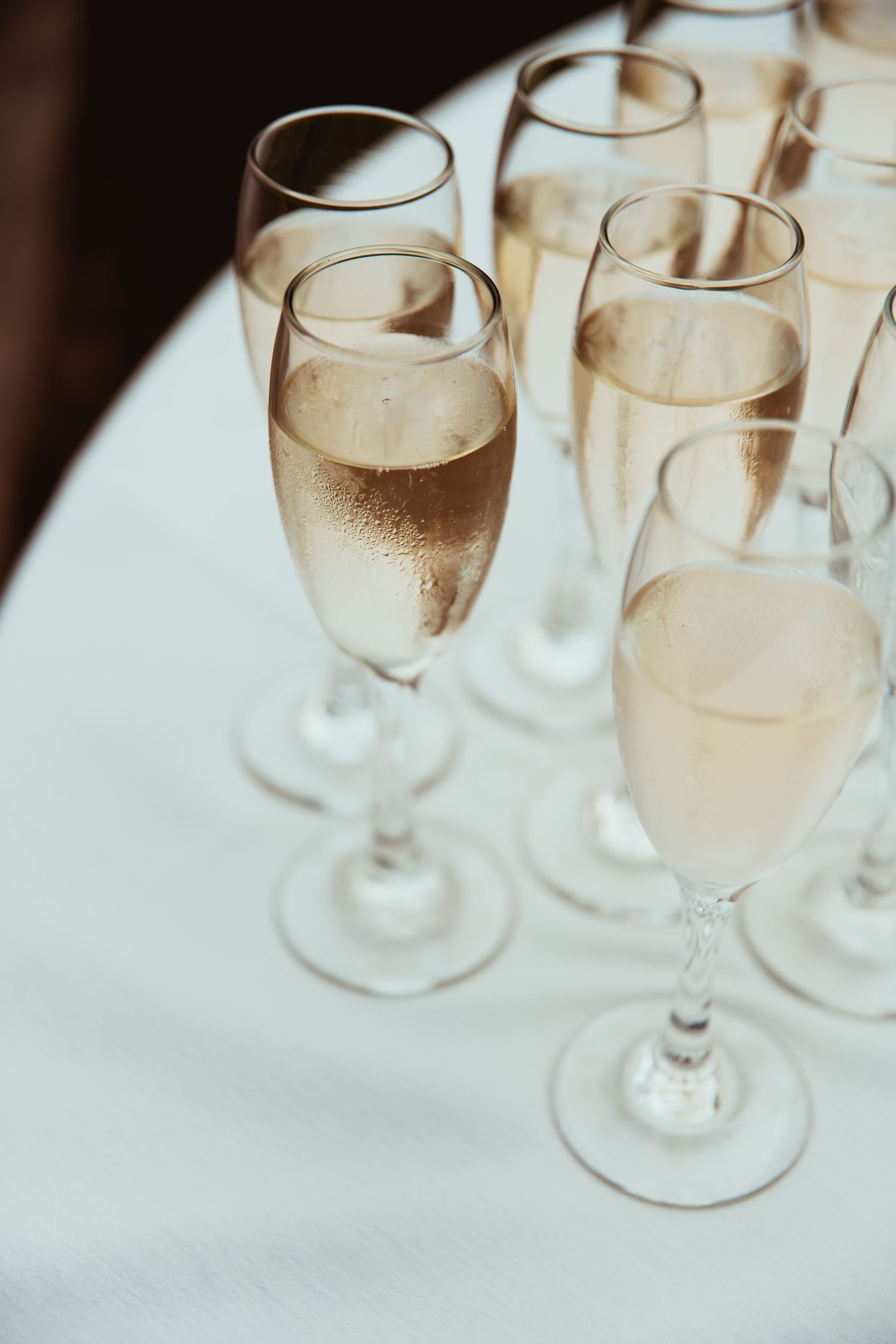 Multiple champagne flutes filled with sparkling wine arranged on a white tablecloth at a wedding reception.