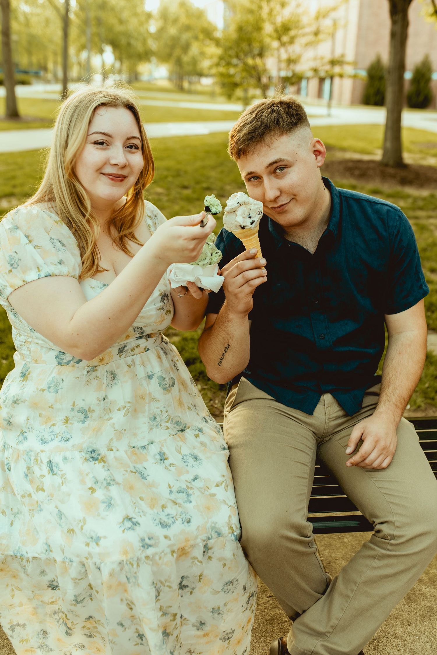 Couple sitting on a bench outdoors, smiling and holding ice cream cones in a park setting.