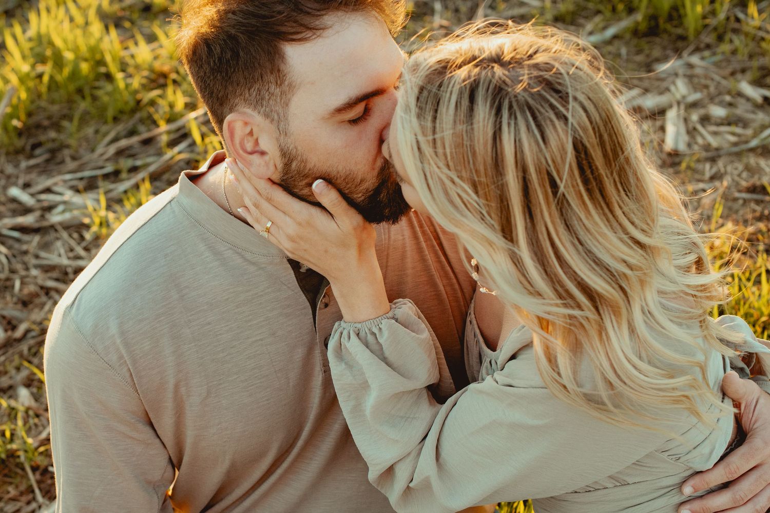 Romantic couple embraces in golden sunlight during outdoor photo session at sunset.