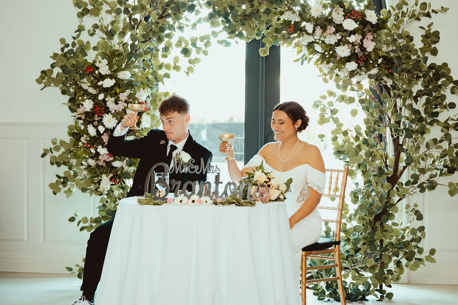 A romantic wedding reception scene with couples dancing and celebrating under elegant greenery decorations.