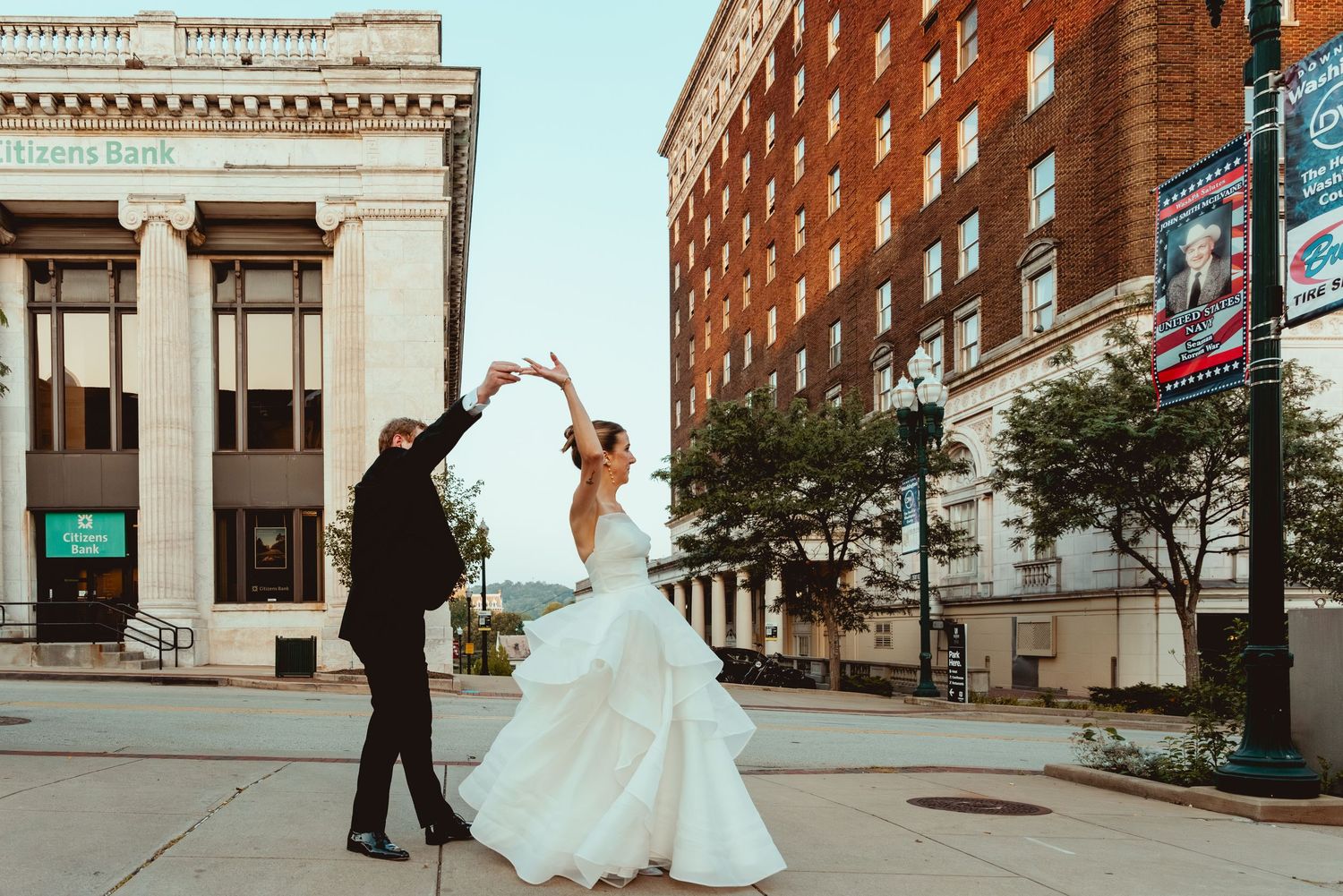 Newlyweds sharing a romantic dance moment outside historic brick building in urban setting.