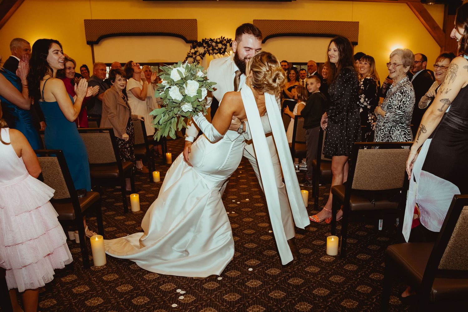 Wedding guests dance and celebrate together on a crowded dance floor at an indoor reception venue.