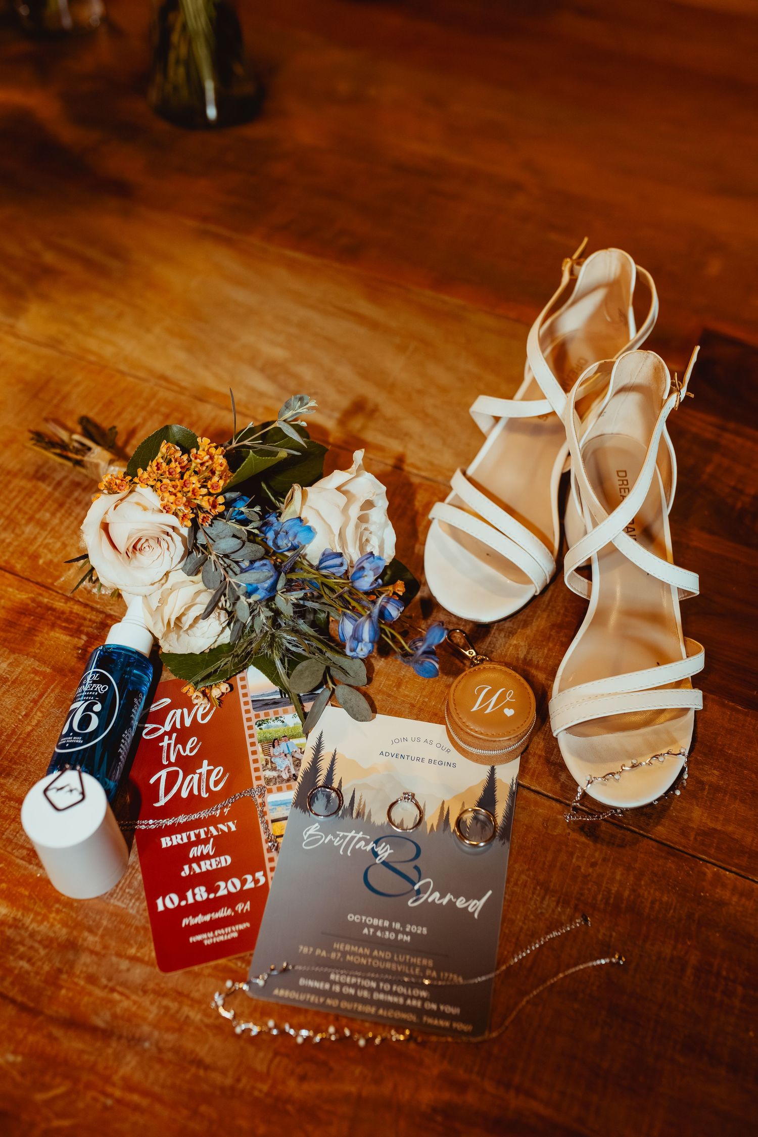 Wedding accessories including white heels, invitation cards with red accents, and delicate blue flowers on wooden surface.