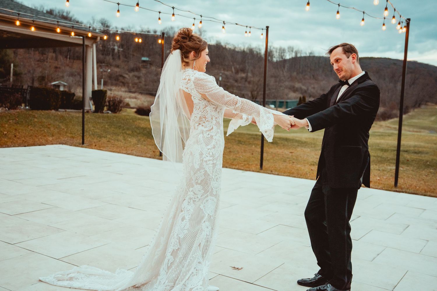 Bride and groom share first dance on outdoor dance floor with string lights and scenic mountain backdrop.