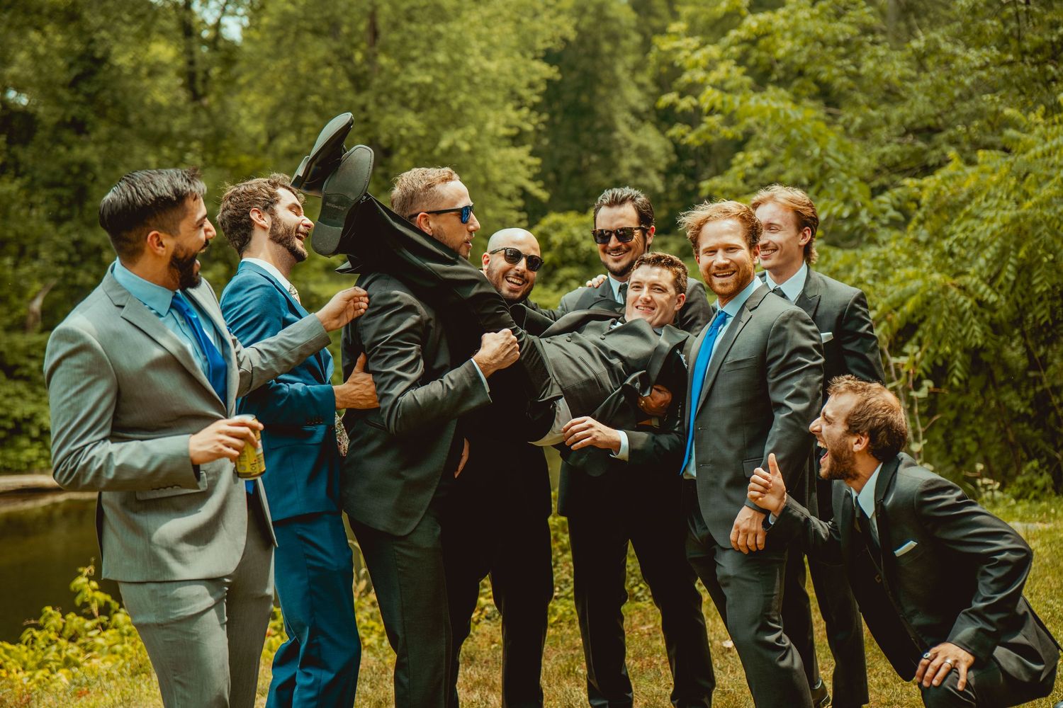 Groomsmen in suits perform celebratory poses during outdoor wedding photo session.