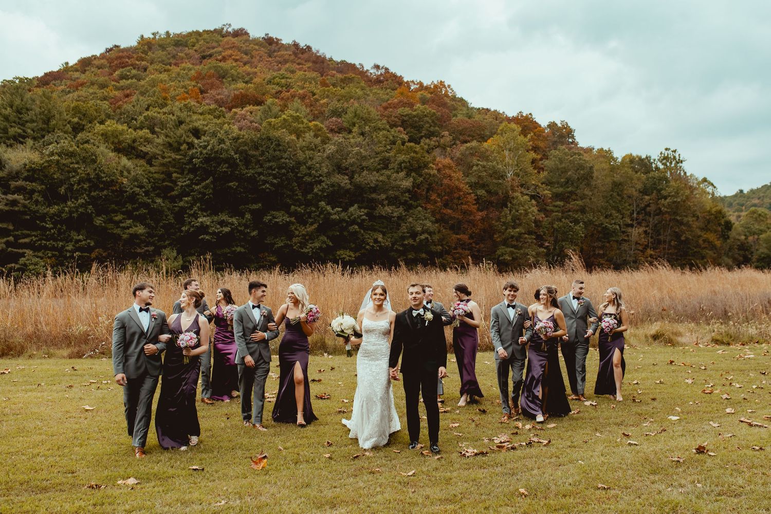 Panoramic view of wedding guests gathered in autumn field with mountain scenery.