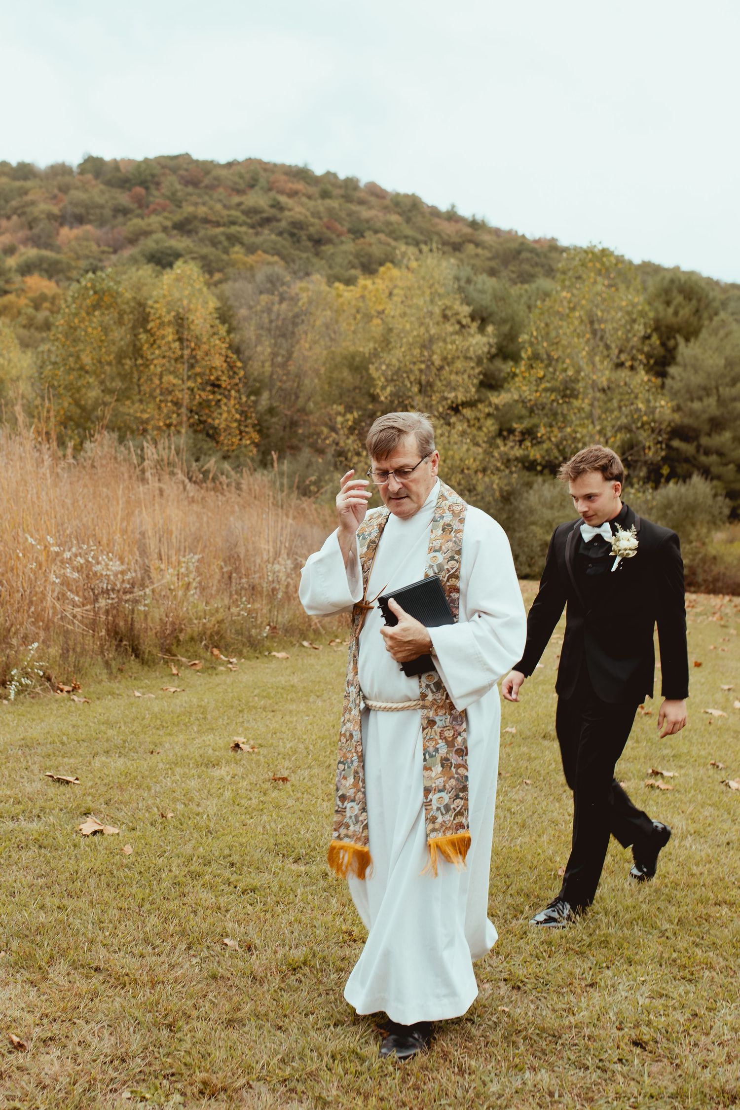 A couple dances playfully in a field surrounded by fall foliage.