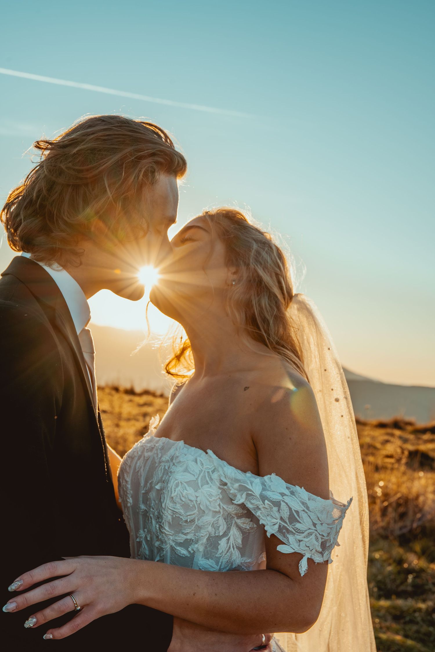 A romantic sunset silhouette of newlyweds sharing a kiss against mountain backdrop.