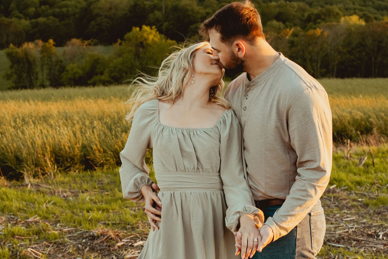 Couple shares intimate moment in rustic outdoor setting with autumn foliage in background.