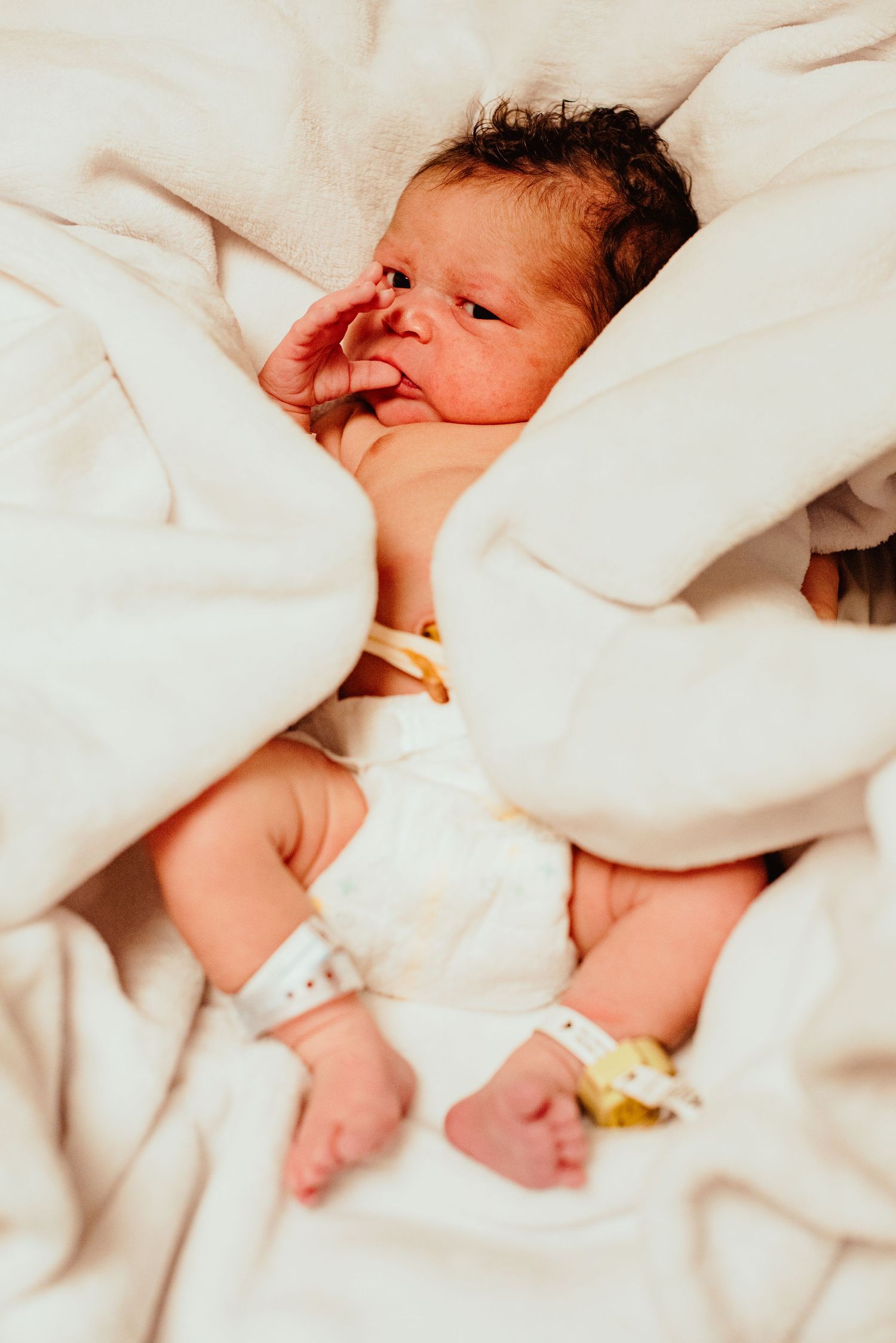 A sleeping newborn baby wrapped in soft white blankets rests peacefully.