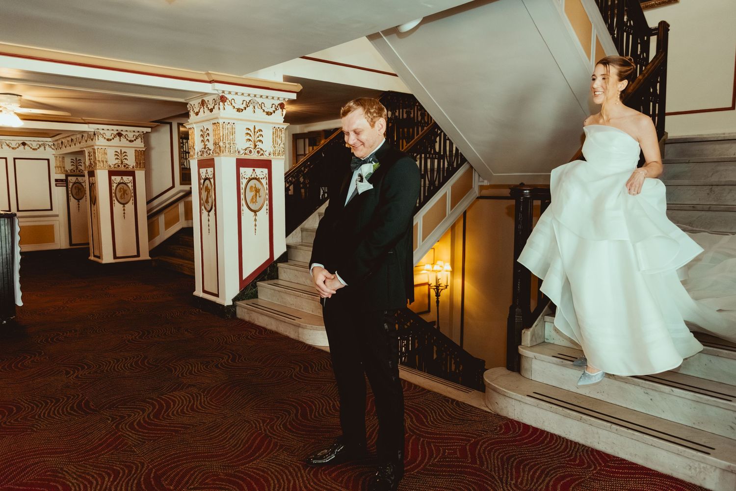 Wedding party reacting with laughter and joy in an ornate indoor venue with decorative columns.
