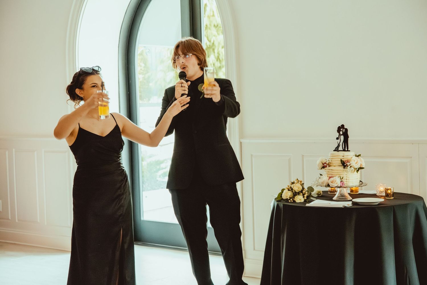 Wedding party members in black formal attire dancing and celebrating at a reception.