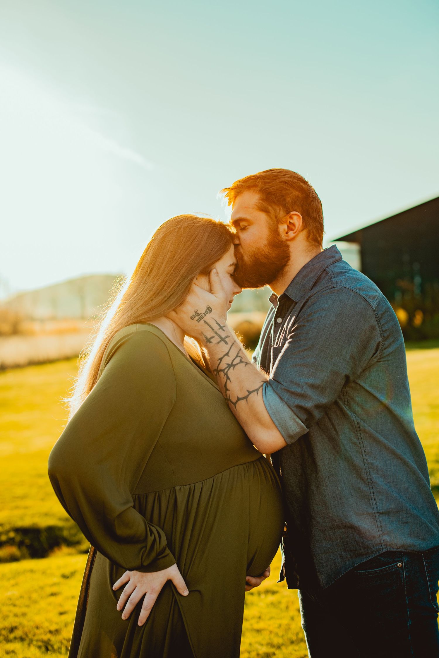 A romantic couple shares tender moments at sunset in a golden field while wearing casual attire.