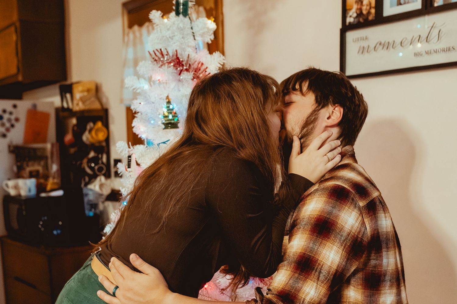 A couple shares an intimate kiss in a warm indoor setting with soft lighting and plaid shirt details.