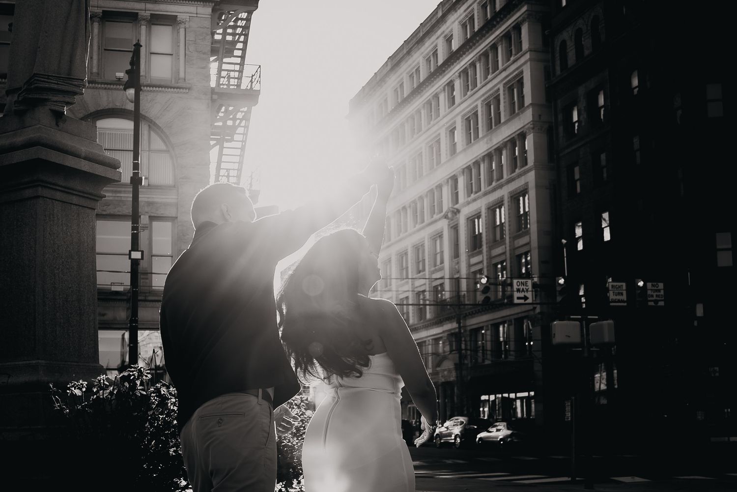 Silhouetted couple embraces in urban setting with dramatic sunlight streaming through buildings.