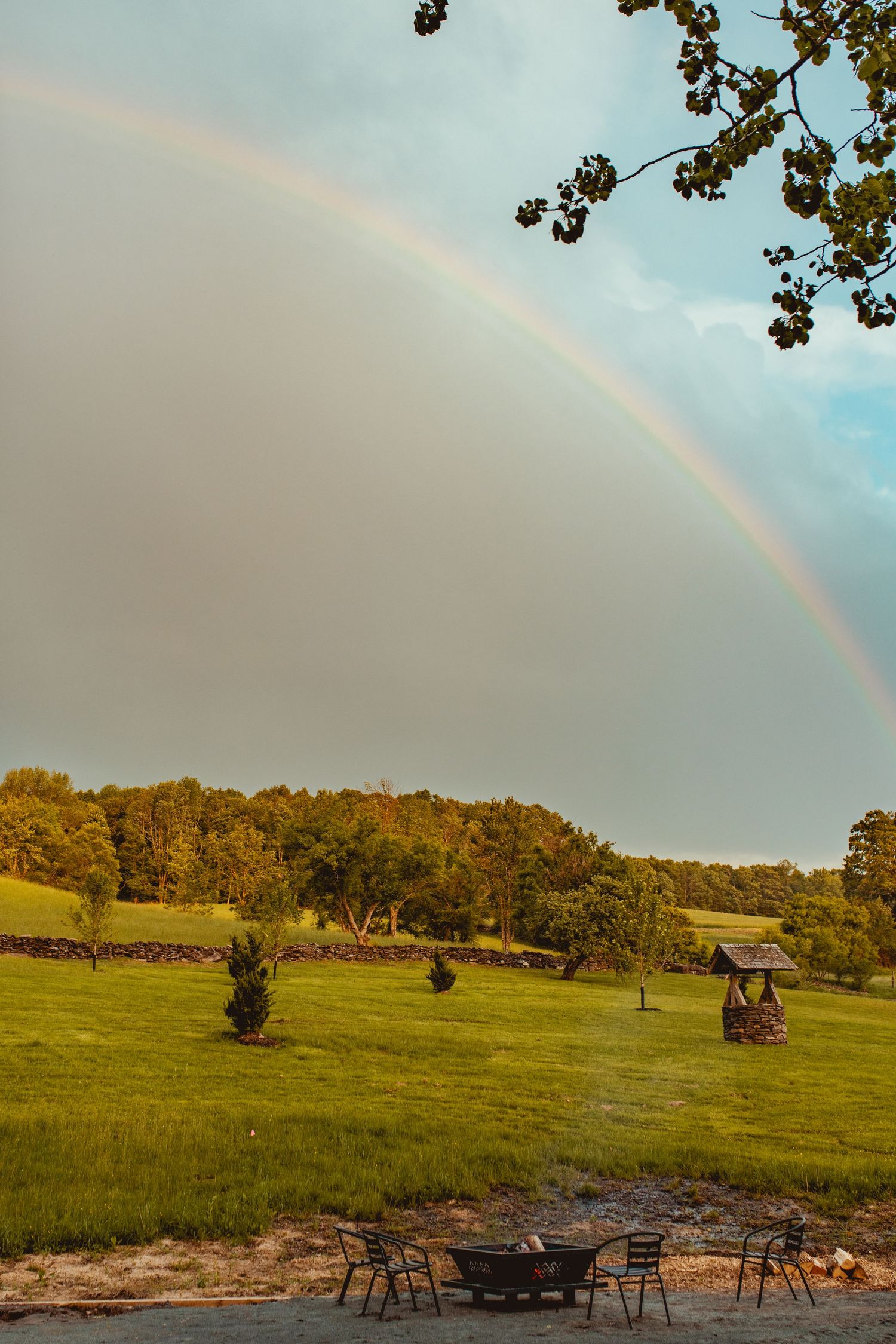 Beautiful double rainbow arches over a green pastoral landscape with scattered trees.