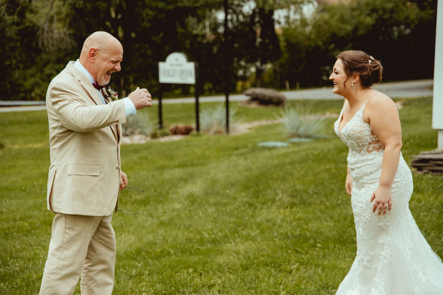 Emotional father reacts seeing bride daughter in wedding dress during first look moment outdoors.